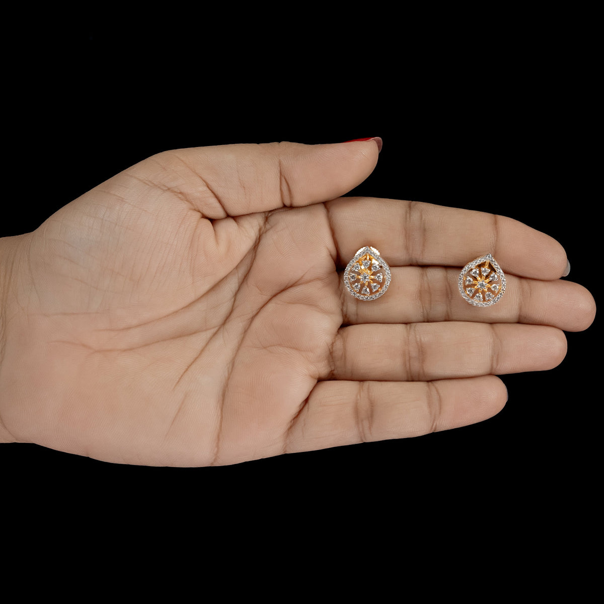 A pair of small round stud earrings with a silver-toned halo and orange stone accents, displayed on an open hand against a solid black background.