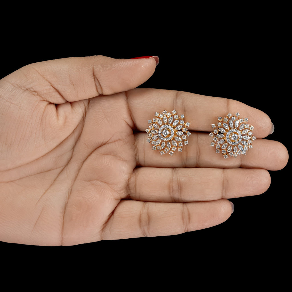 A pair of round cluster stud earrings with clear stones in a gold-tone setting, displayed on an open hand against a solid black background.