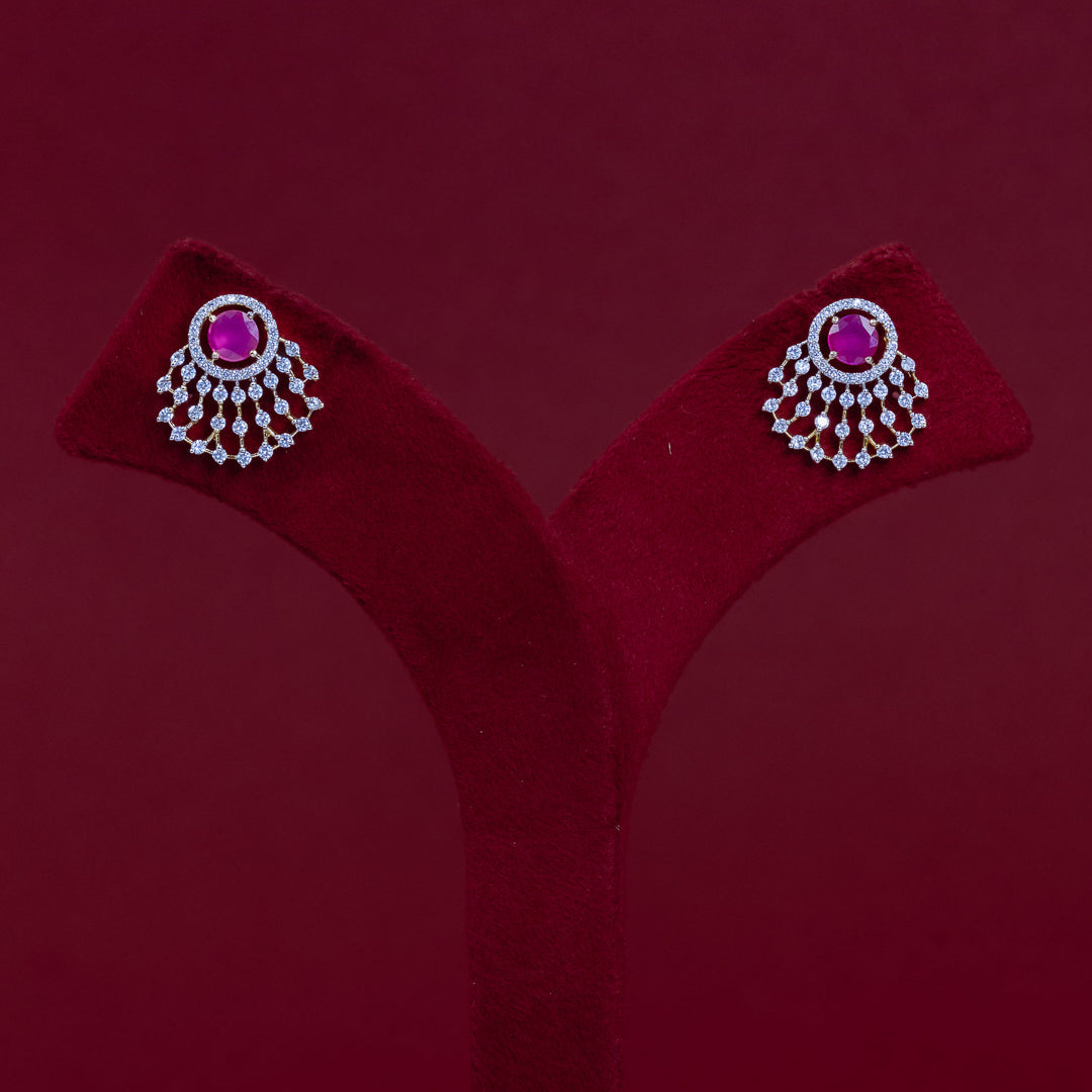 A pair of silver-toned statement earrings with round pink gemstones and dangling crystal-like accents, displayed on a red velvet jewelry stand against a dark red background.