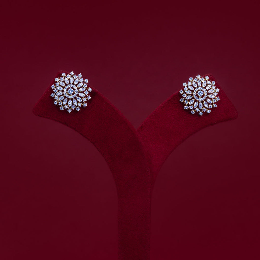 A pair of round floral stud earrings with clear gemstones in a silver-toned setting, displayed on a red velvet jewelry stand against a dark red background.