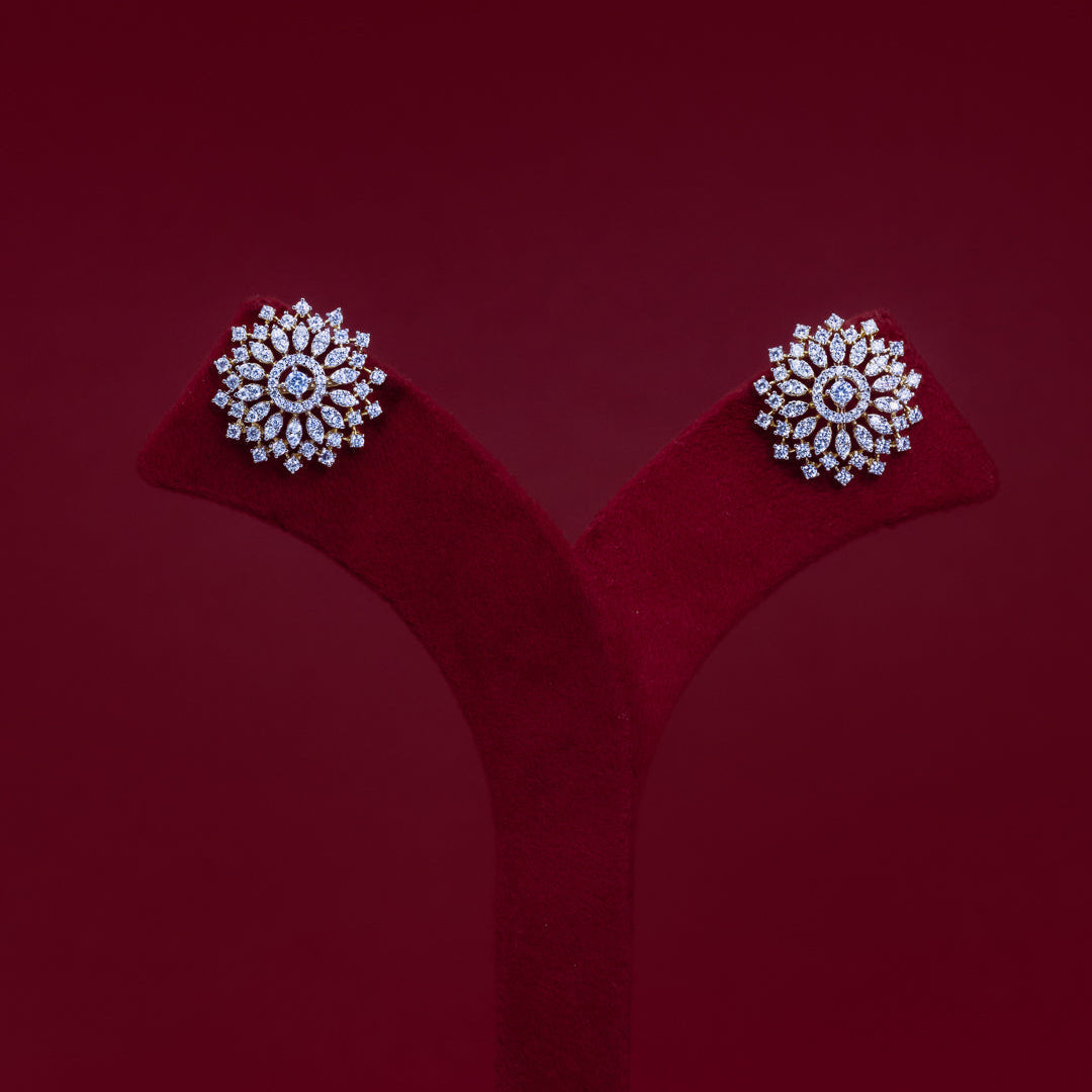 A pair of round floral stud earrings with clear gemstones in a silver-toned setting, displayed on a red velvet jewelry stand against a dark red background.